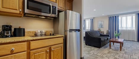 A kitchen with wooden cabinets, a stainless steel refrigerator, and a microwave. There is a dining area with a sofa and a table.