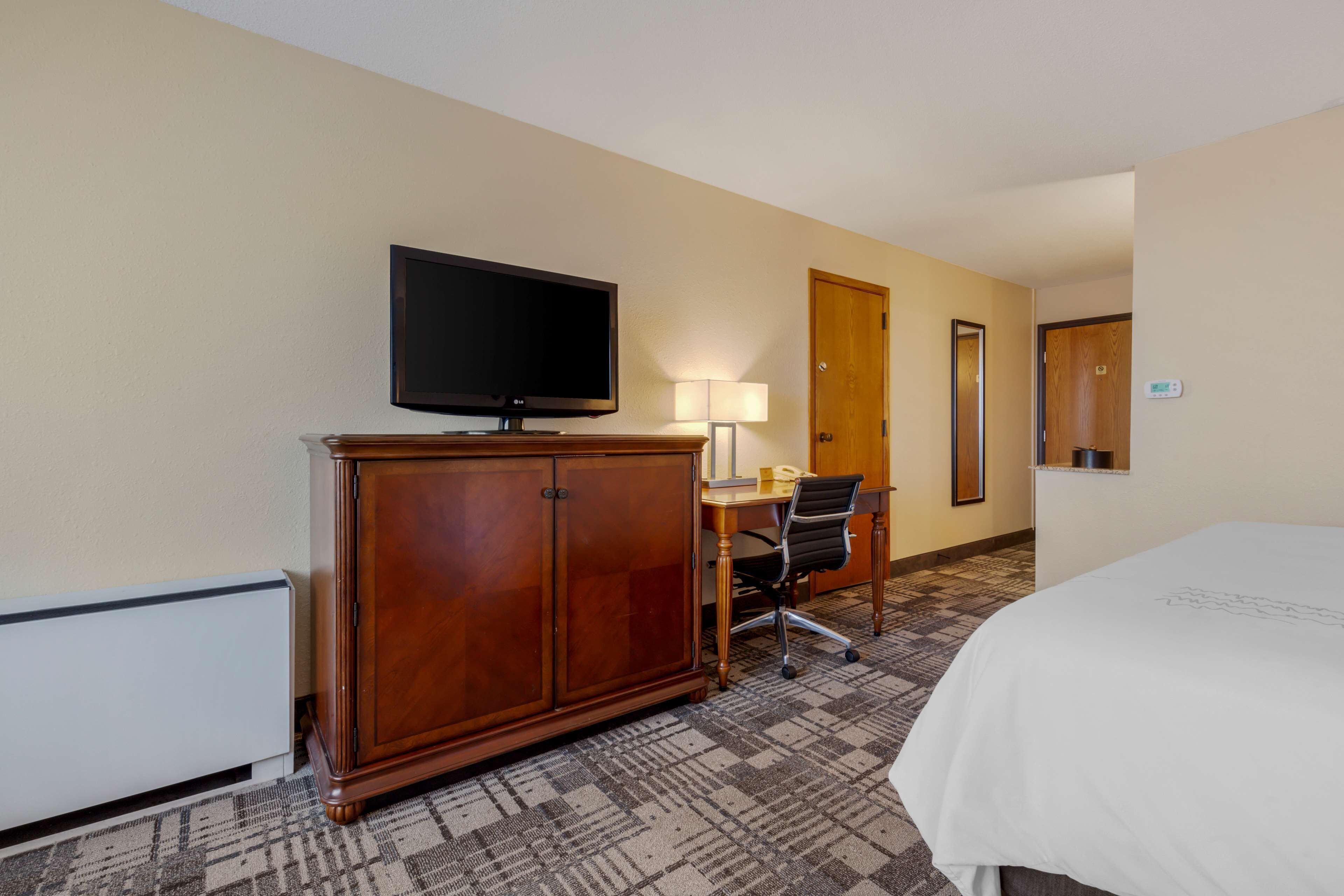 A hotel room with a large bed, a wooden cabinet, a desk with a chair, a television, and a door.