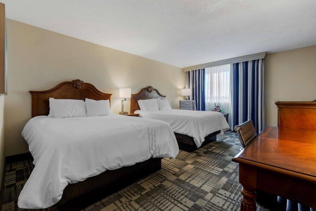 A hotel room with two beds, a wooden headboard, a desk, and a patterned carpet.