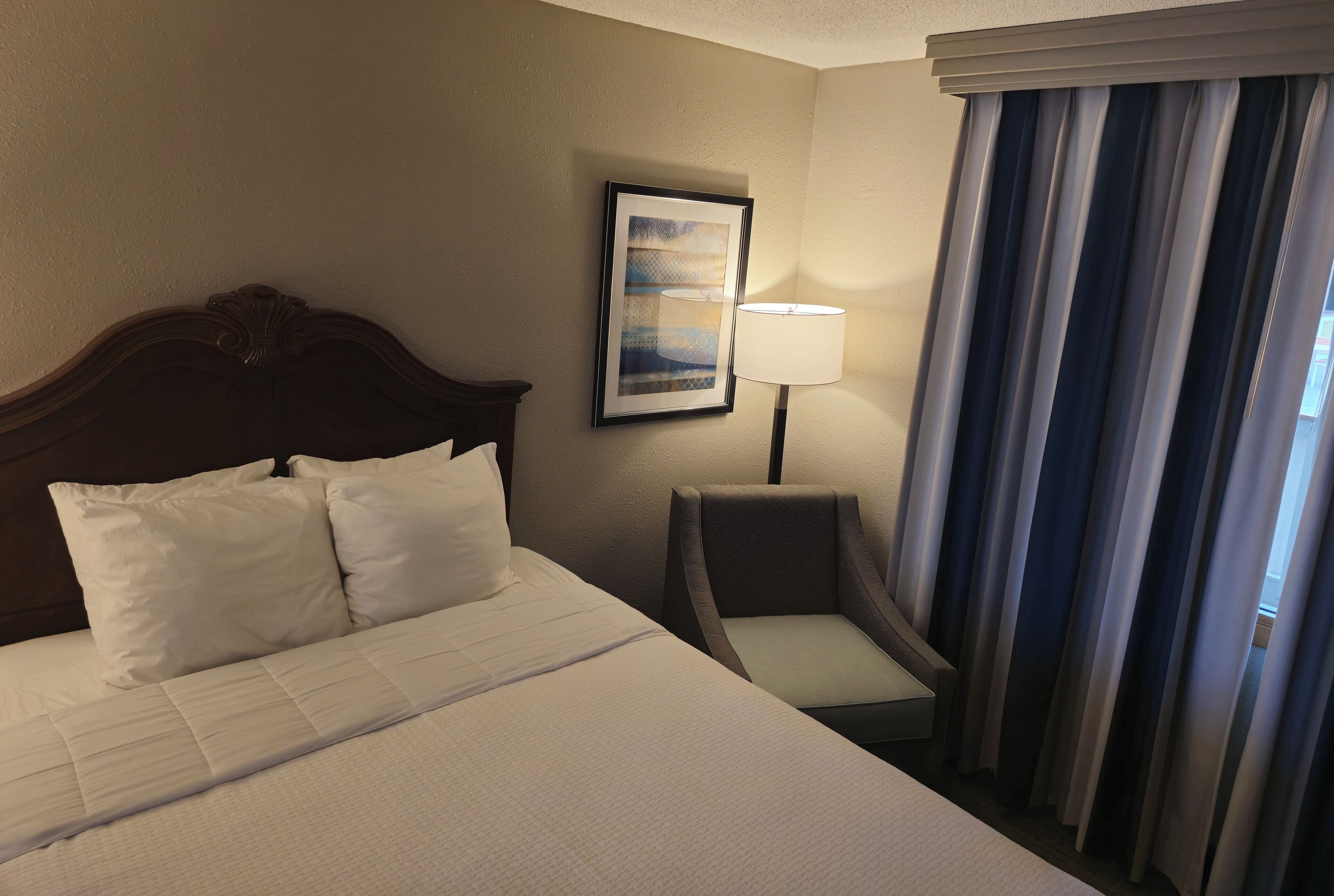A hotel room with a large bed, a chair, a lamp, and a painting on the wall.