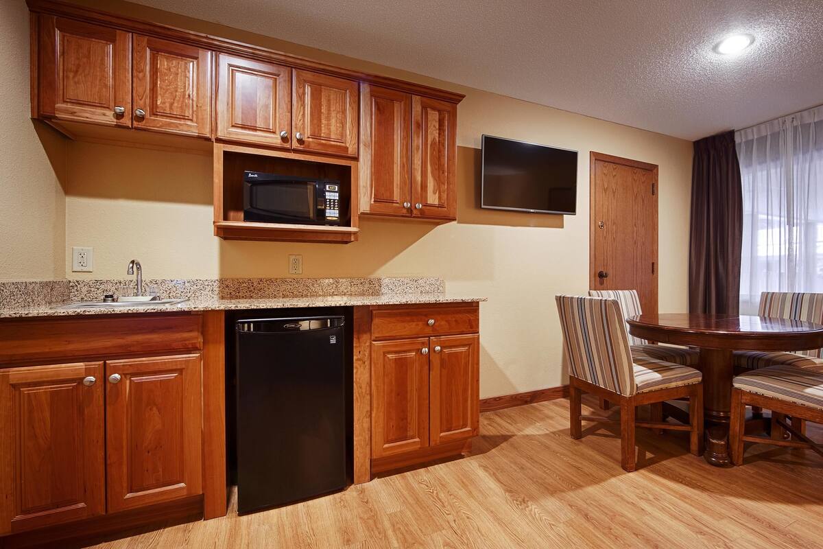 A kitchen with wooden cabinets, a microwave, and a dishwasher. There is a dining table with chairs and a TV mounted on the wall.
