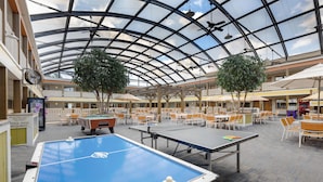 Un grand espace intérieur comprenant une table de billard, une table de ping-pong, ainsi que plusieurs tables et chaises.