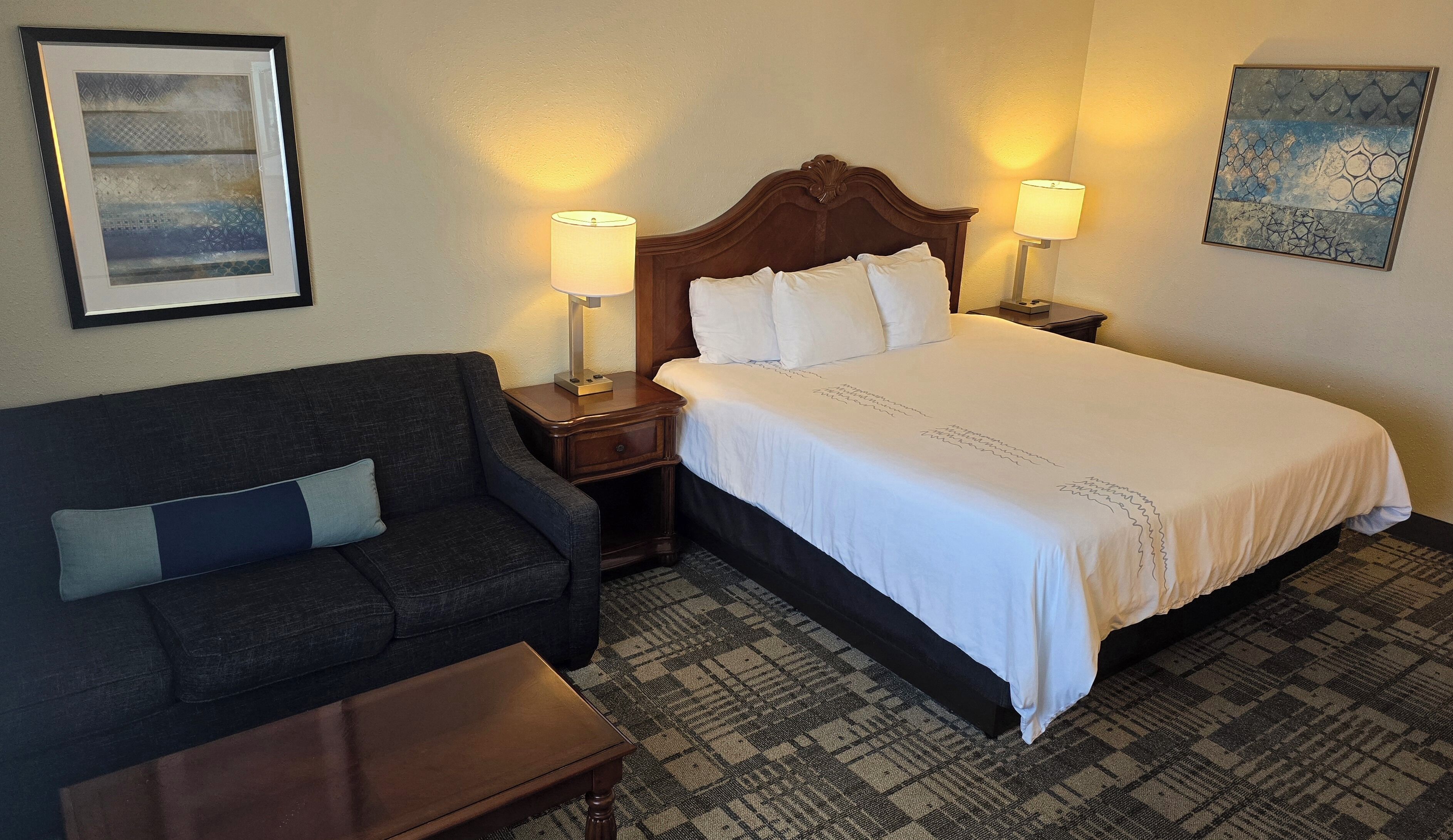 A hotel room with a bed, a sofa, a nightstand, and a lamp.