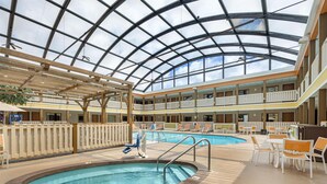 Un atrium d’hôtel avec un plafond en verre, deux piscines et des espaces de détente en plein air.