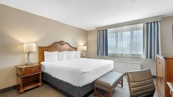 A hotel room with a large bed, bedside tables, a chair, a desk, and a window with curtains.