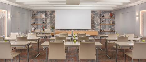 A conference room with tables, chairs, a projector screen, and shelves with decorative items.