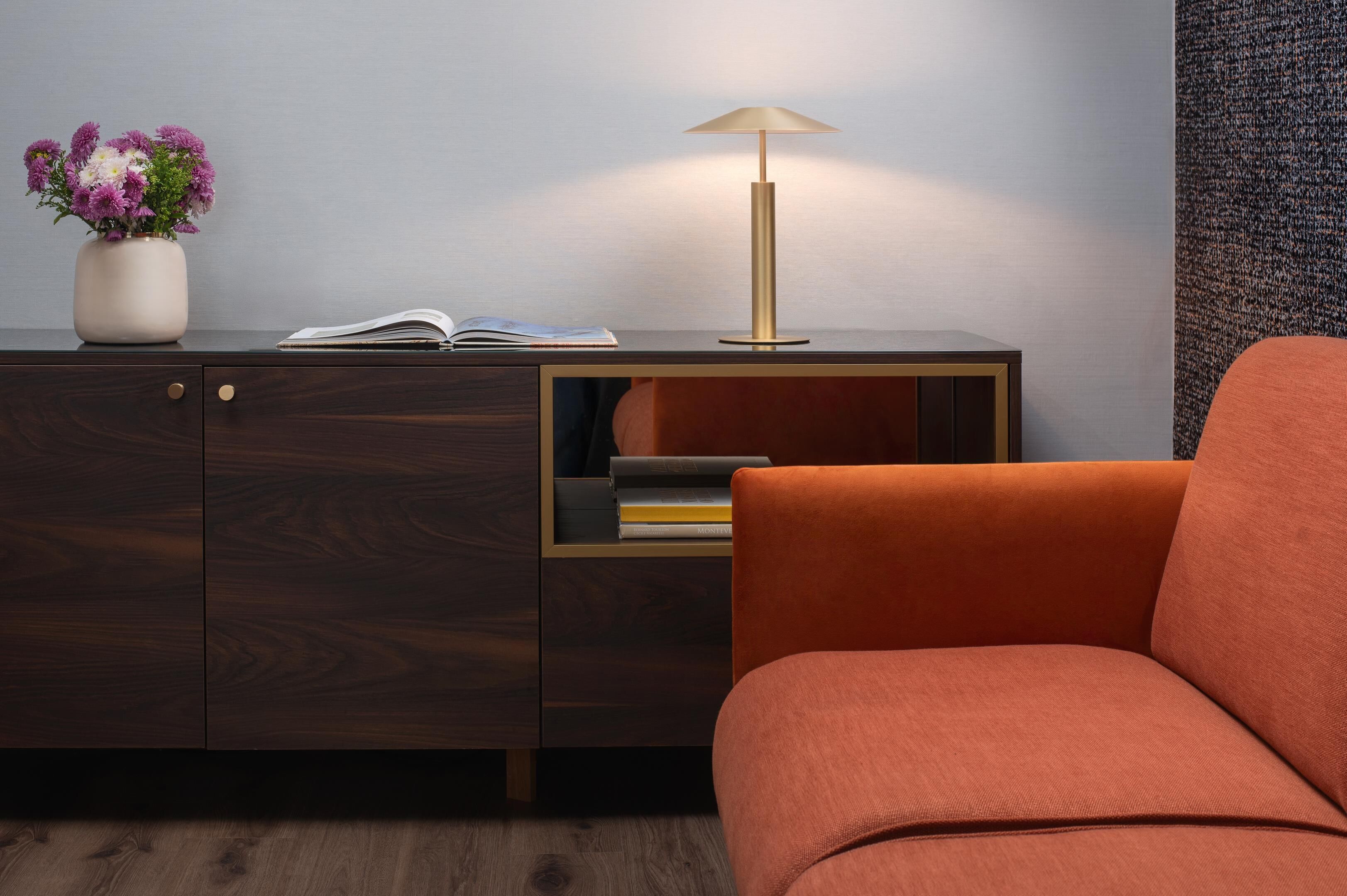 Ein modernes Zimmer mit einem Holzschrank, einer Vase mit Blumen, einer Lampe und einem roten Stuhl.