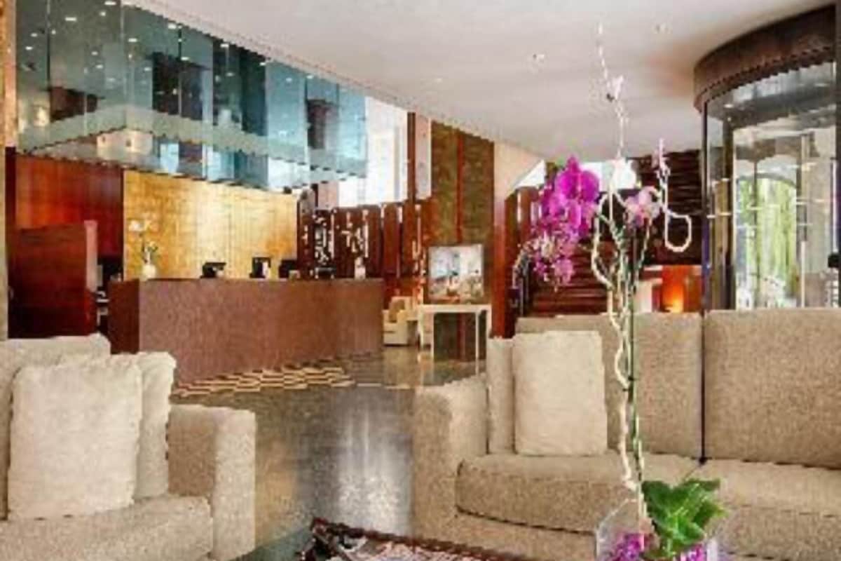 A hotel lobby with a reception desk, sofas, a coffee table with magazines, and a decorative orchid vase.