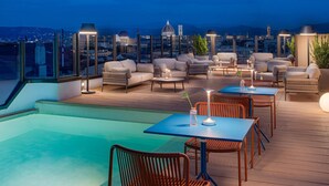 Un bar en la azotea con piscina, mobiliario exterior y vistas a la ciudad.