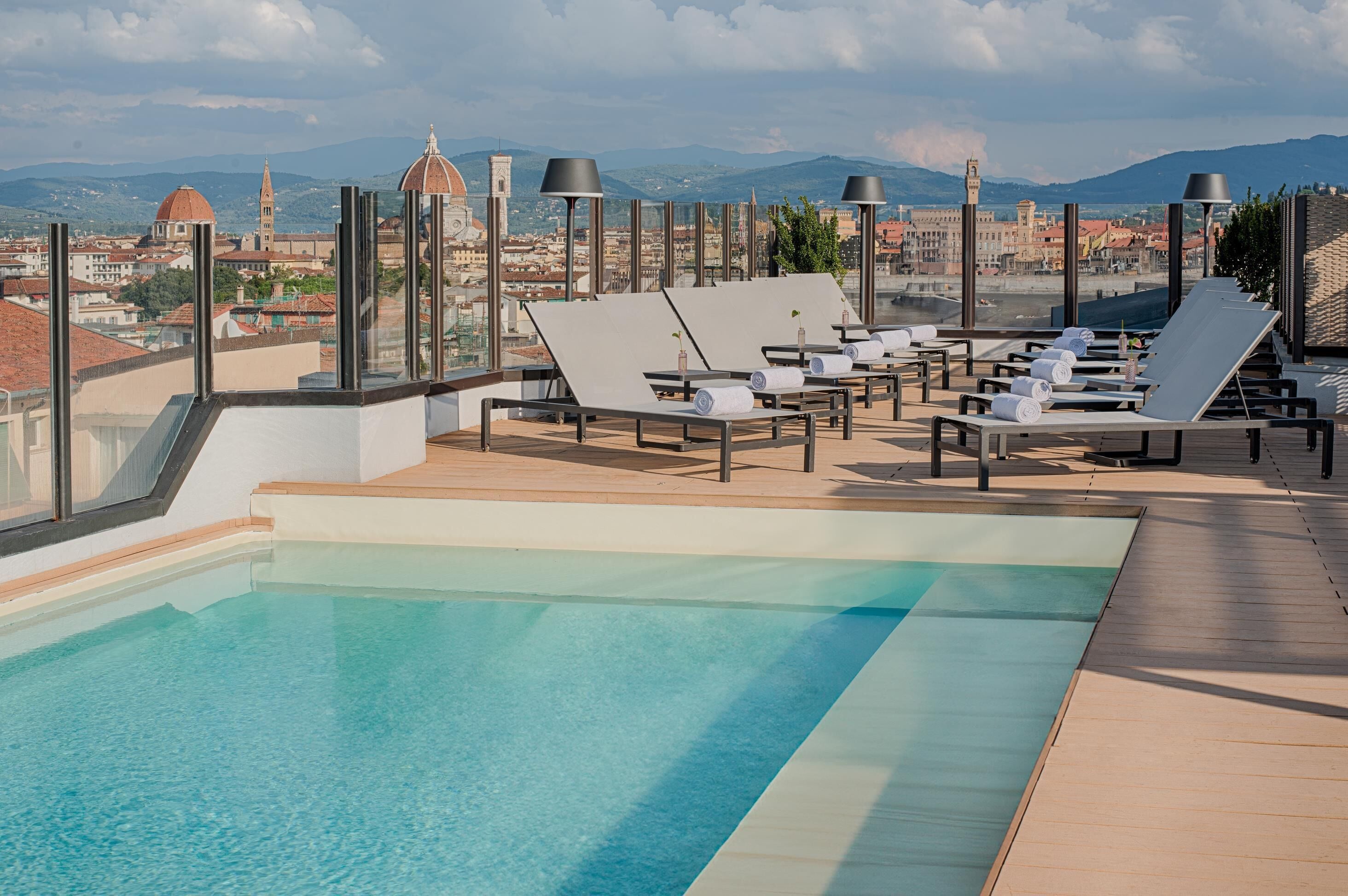 Una piscina en la azotea con sillones de descanso y vistas a un paisaje urbano.