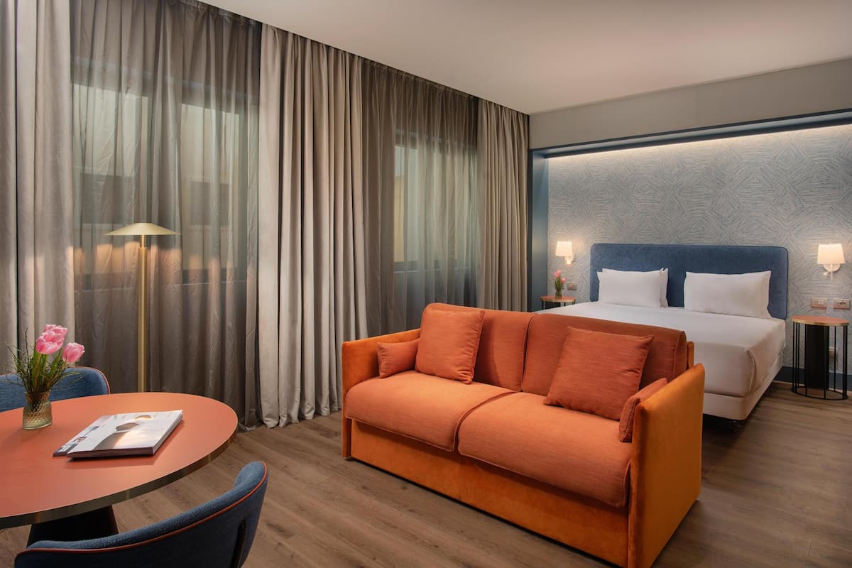 A hotel room with a bed, a sofa, a round table, and a lamp.