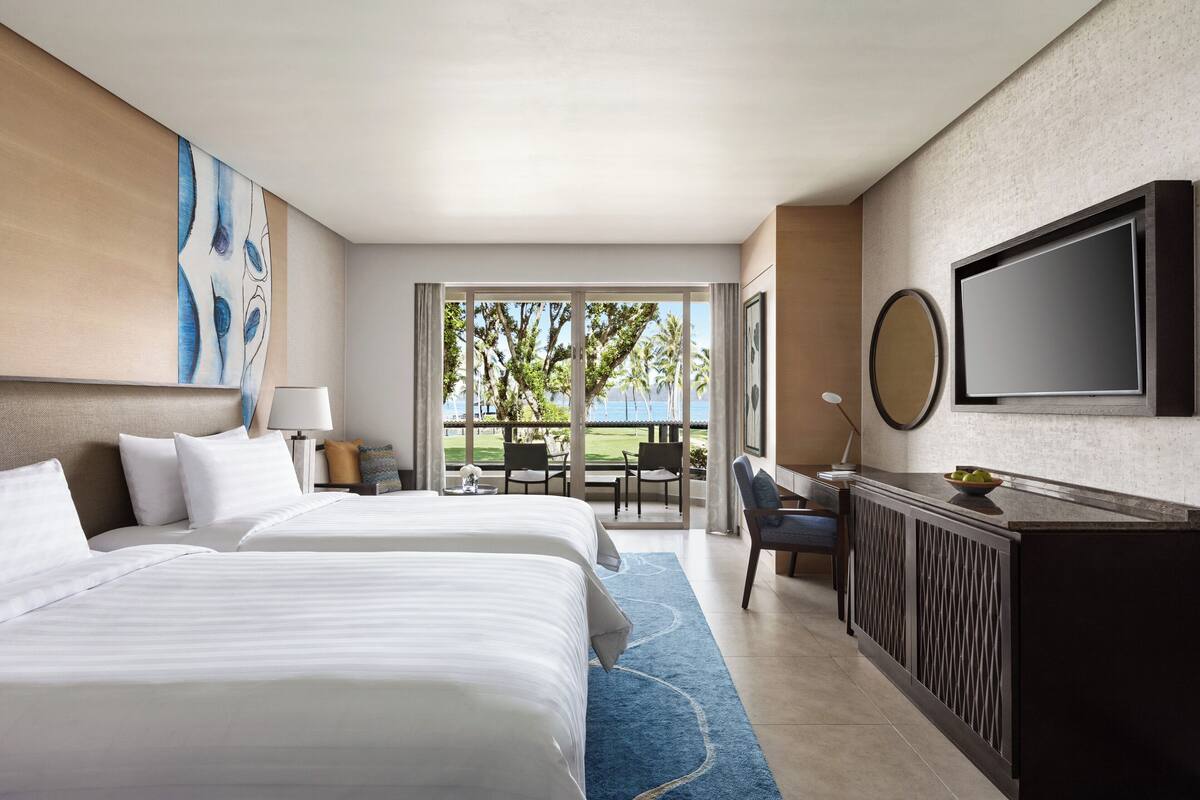 A hotel room with two beds, a TV, a desk, and a view of the outdoors.