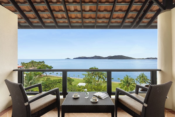 A balcony with wicker furniture, a table with a book and a cup, and a view of the sea and greenery. - Shangri-La Tanjung Aru, Kota Kinabalu (Kota Kinabalu)