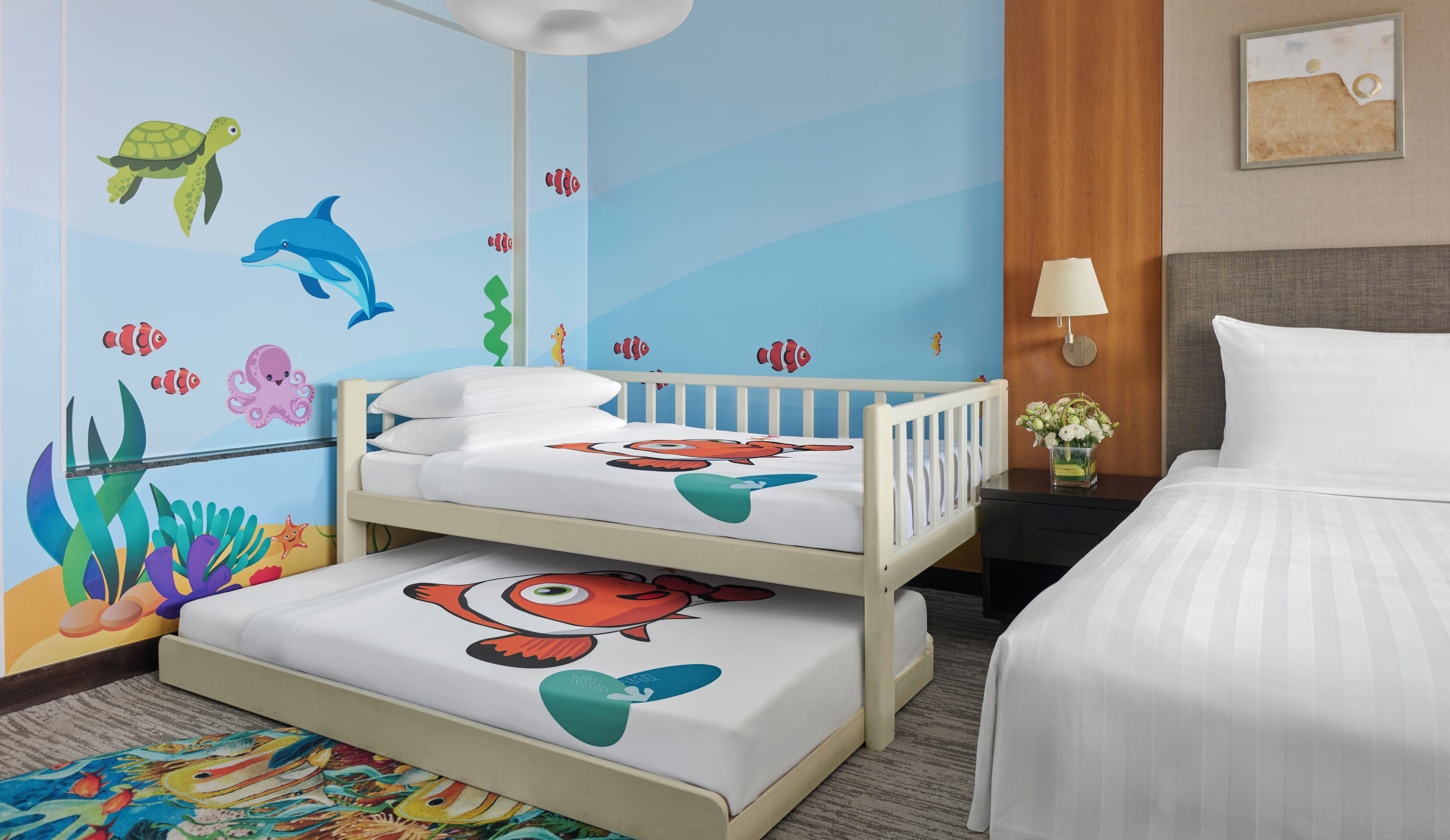A child's room with a bunk bed, a bed, a nightstand, and a wall mural of sea creatures.