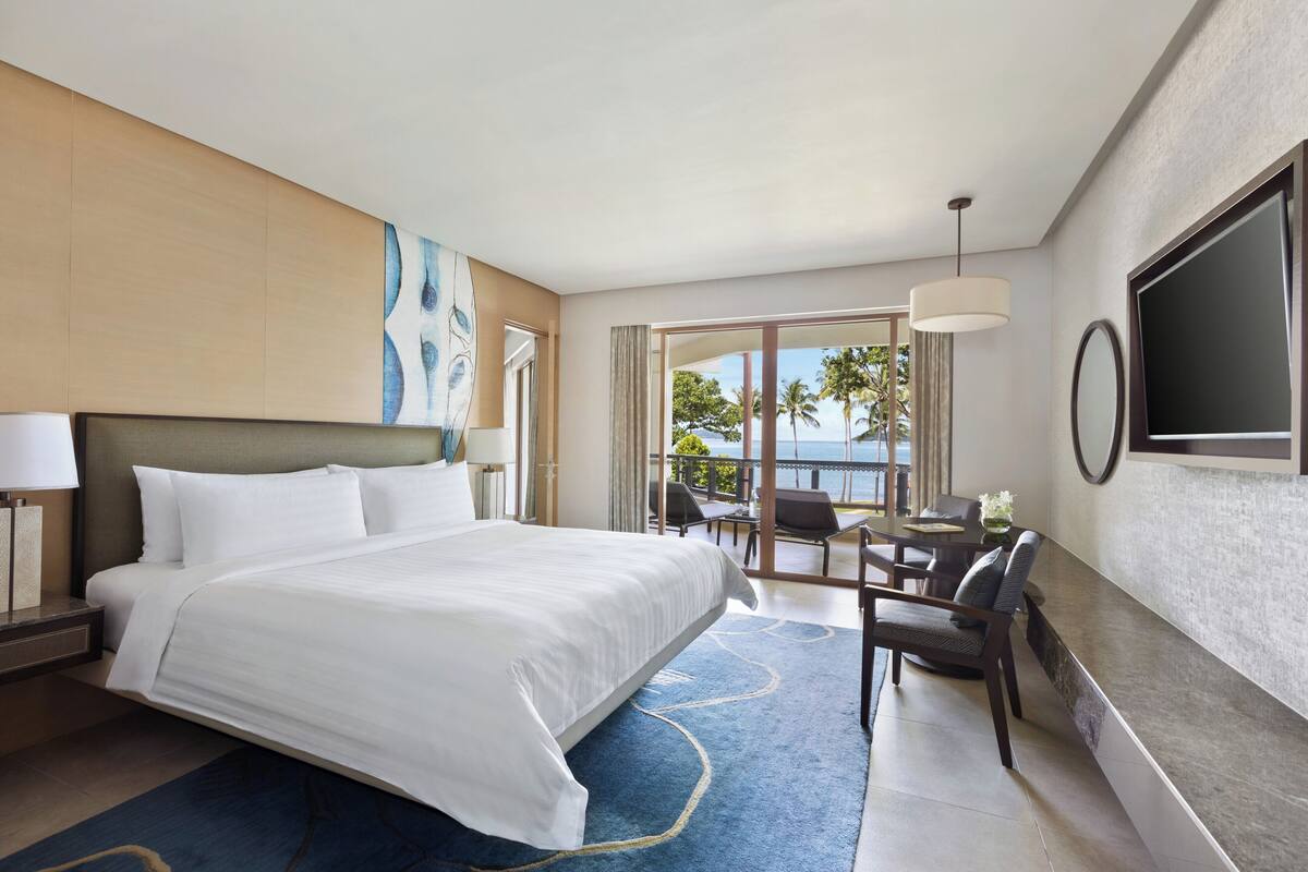 A hotel room with a large bed, a desk with a chair, a TV, and a view of the outdoors.