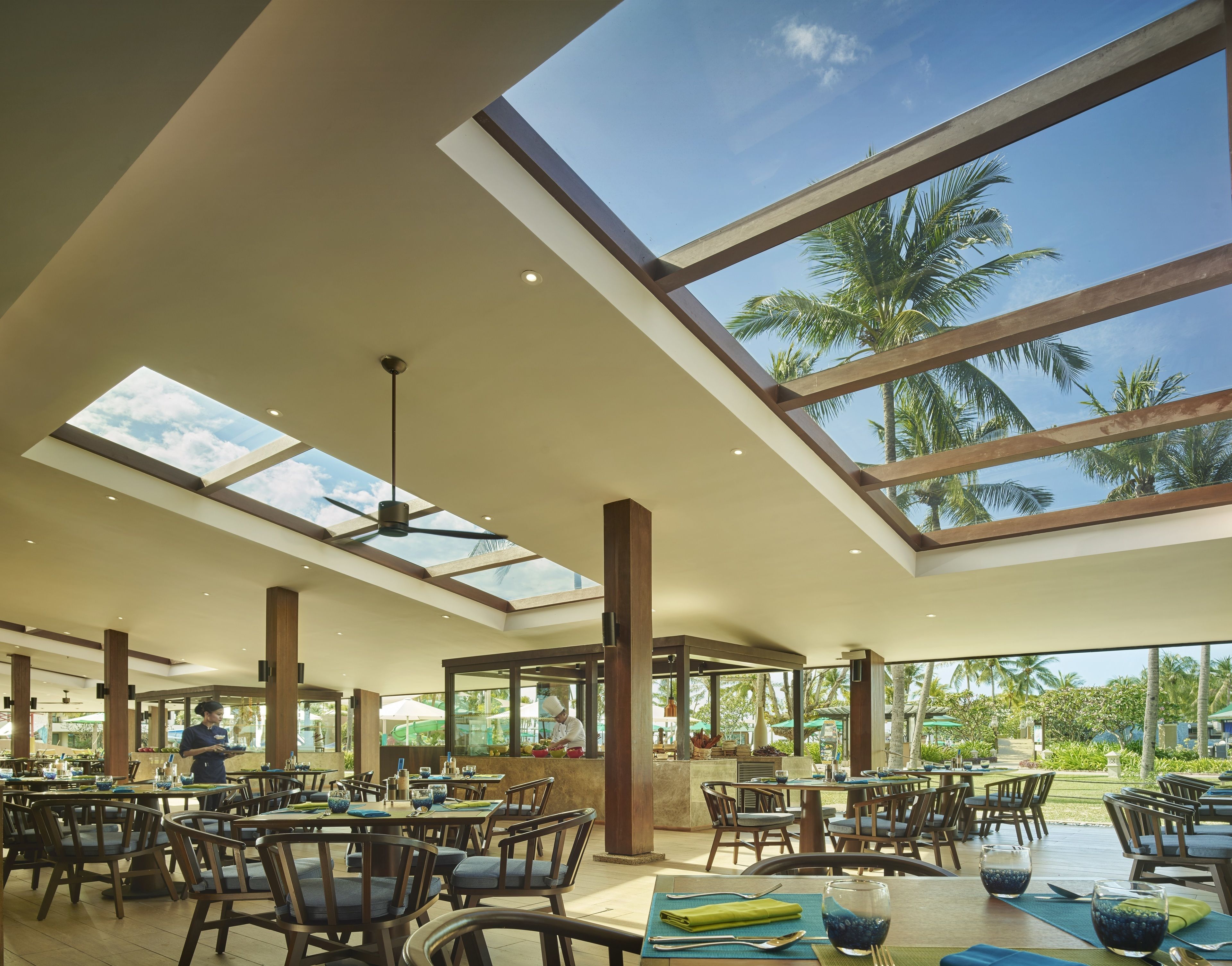 A spacious restaurant with high ceilings, large windows, and a view of palm trees.