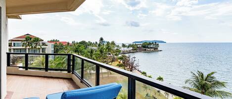A balcony with wicker chairs, a view of the sea, and a distant island.