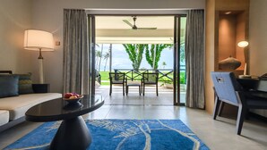 Habitación de hotel con sofá, mesa de comedor, una silla, lámpara y vista a un césped y palmeras a través de la puerta de vidrio.