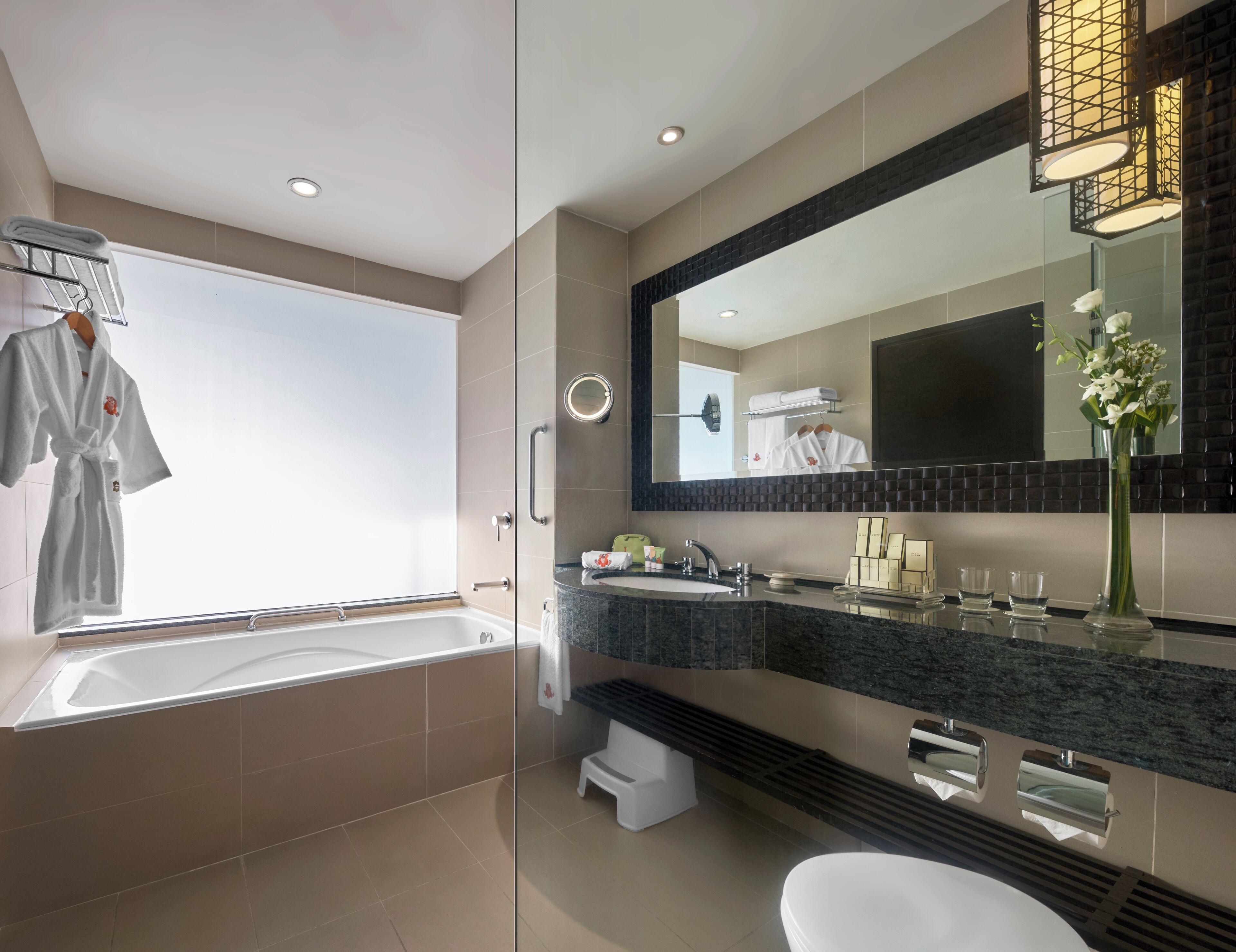 Une salle de bain moderne avec une baignoire, un grand miroir, un meuble-lavabo et des toilettes.