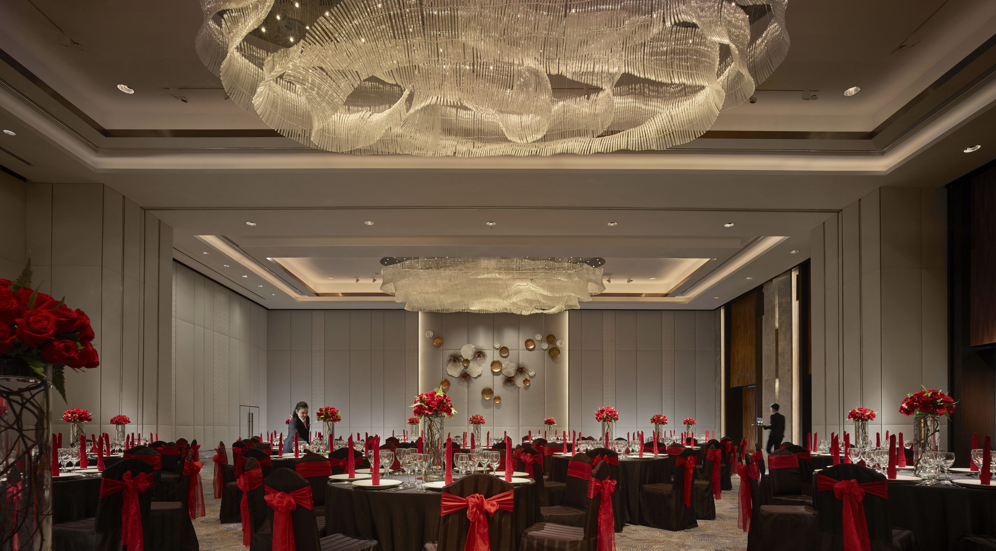 A banquet hall with round tables, red sashes, and a large chandelier.