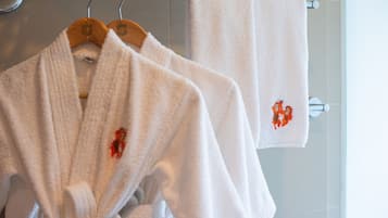 Deux peignoirs blancs sont suspendus à un porte-serviettes en métal, et une serviette est posée sur une barre à serviettes fixée au mur.