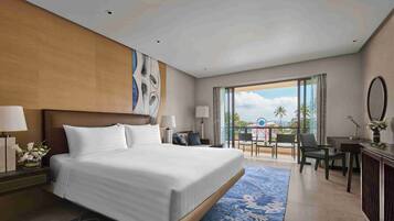 A hotel room with a large bed, a desk, a chair, and a balcony with a view of palm trees.