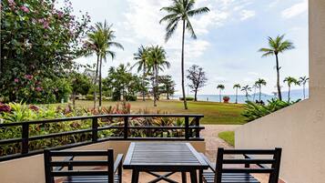 A patio with a table and chairs, overlooking a landscaped area with palm trees and a view of the ocean.