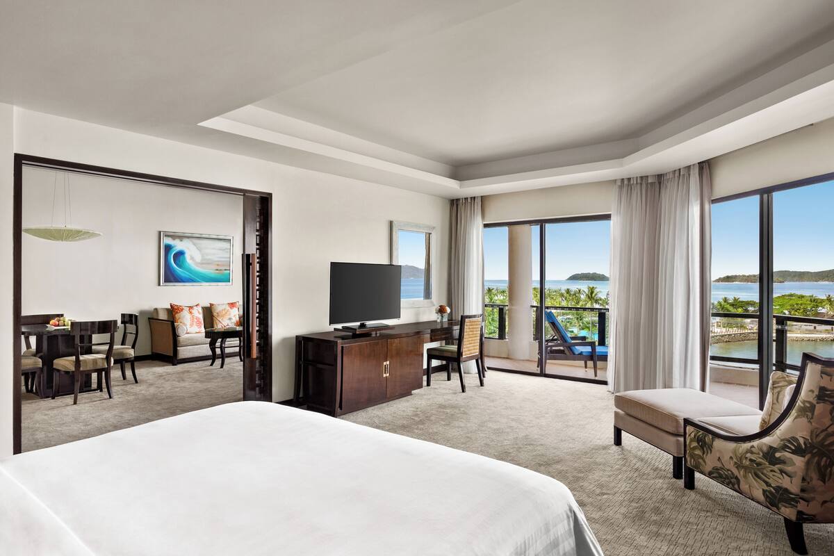 A hotel room with a large bed, a desk, a TV, and a view of the ocean.