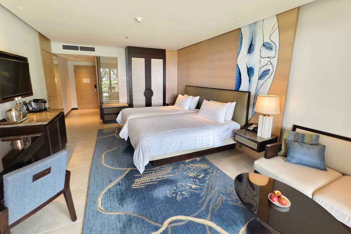 A hotel room with a large bed, a desk with a television, a sofa, and a dining table with apples.
