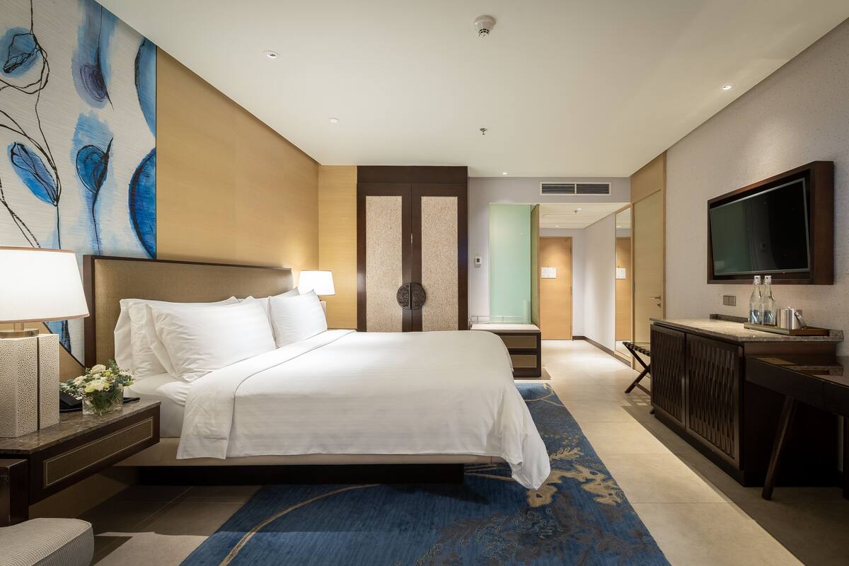 A hotel room with a large bed, a TV, a desk, and a bathroom visible through an open door.