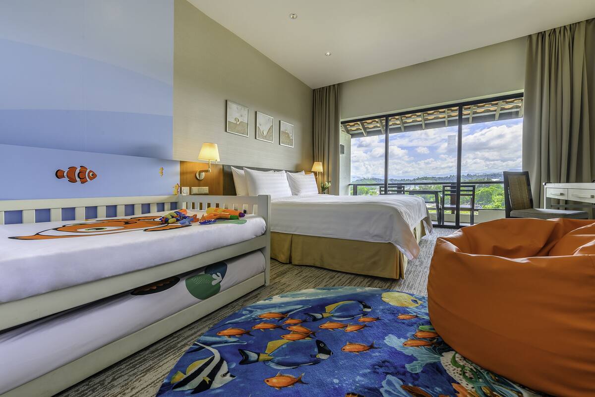 A hotel room with a bed, a sofa, a bean bag, and a balcony with a view.