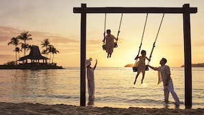 Escena de playa con un columpio, palmeras y un atardecer.
