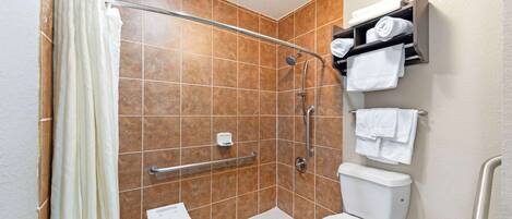 A bathroom with a shower, toilet, and a small table with a chair.