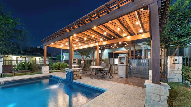 A covered outdoor pool area with a pergola, stone pillars, and a small waterfall feature. - Best Western Post Oak Inn (Burnet)