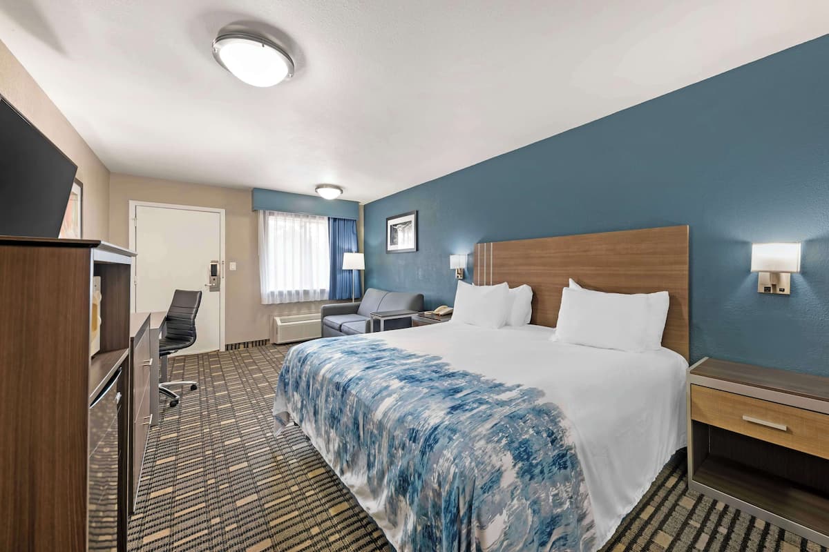 A hotel room with a large bed, a desk, a chair, a desk lamp, and a nightstand.