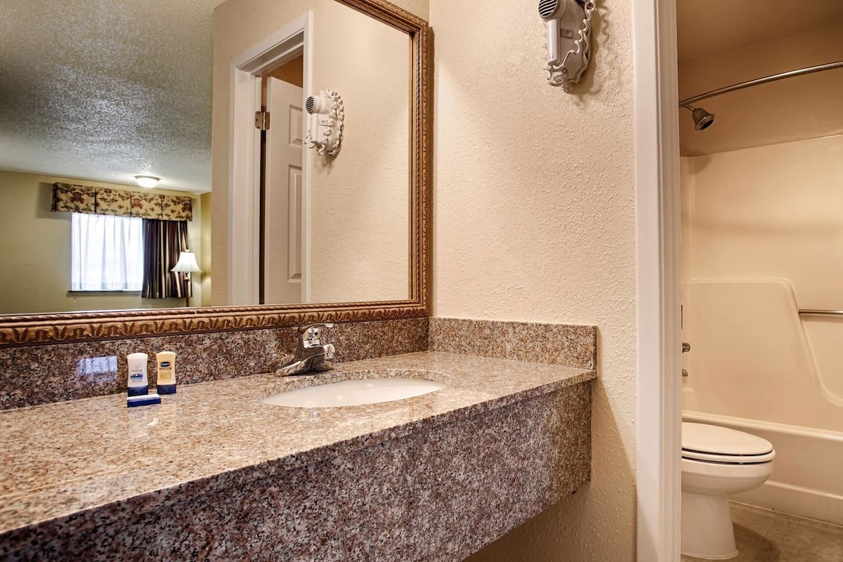 A bathroom with a granite countertop, a sink, a mirror, a hairdryer, and a bathtub.