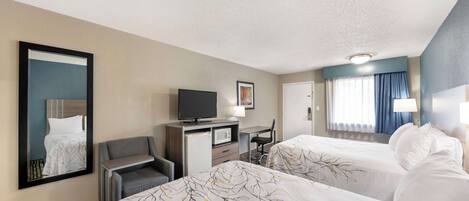 A hotel room with two beds, a desk with a television, a small seating area, and a large mirror.