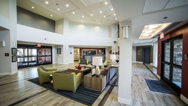 A spacious lobby with a high ceiling, modern lighting, and a central seating area with sofas and a coffee table.
