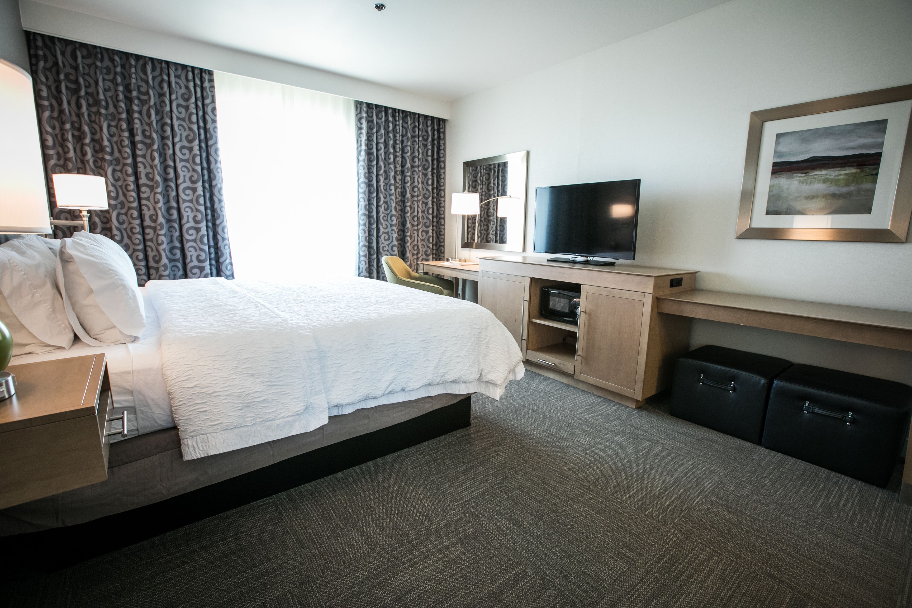 Habitación de hotel con una cama grande, un escritorio con televisor, una silla y una pequeña zona de estar.