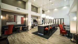 A spacious hotel lobby with a long reception desk, multiple seating areas, and a high ceiling with recessed lighting.
