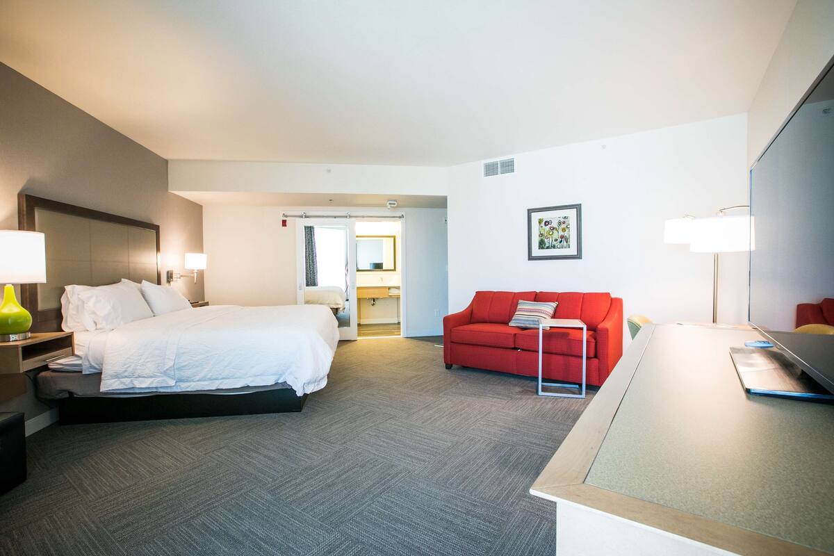 A hotel room with a bed, a red sofa, a desk, and a TV.