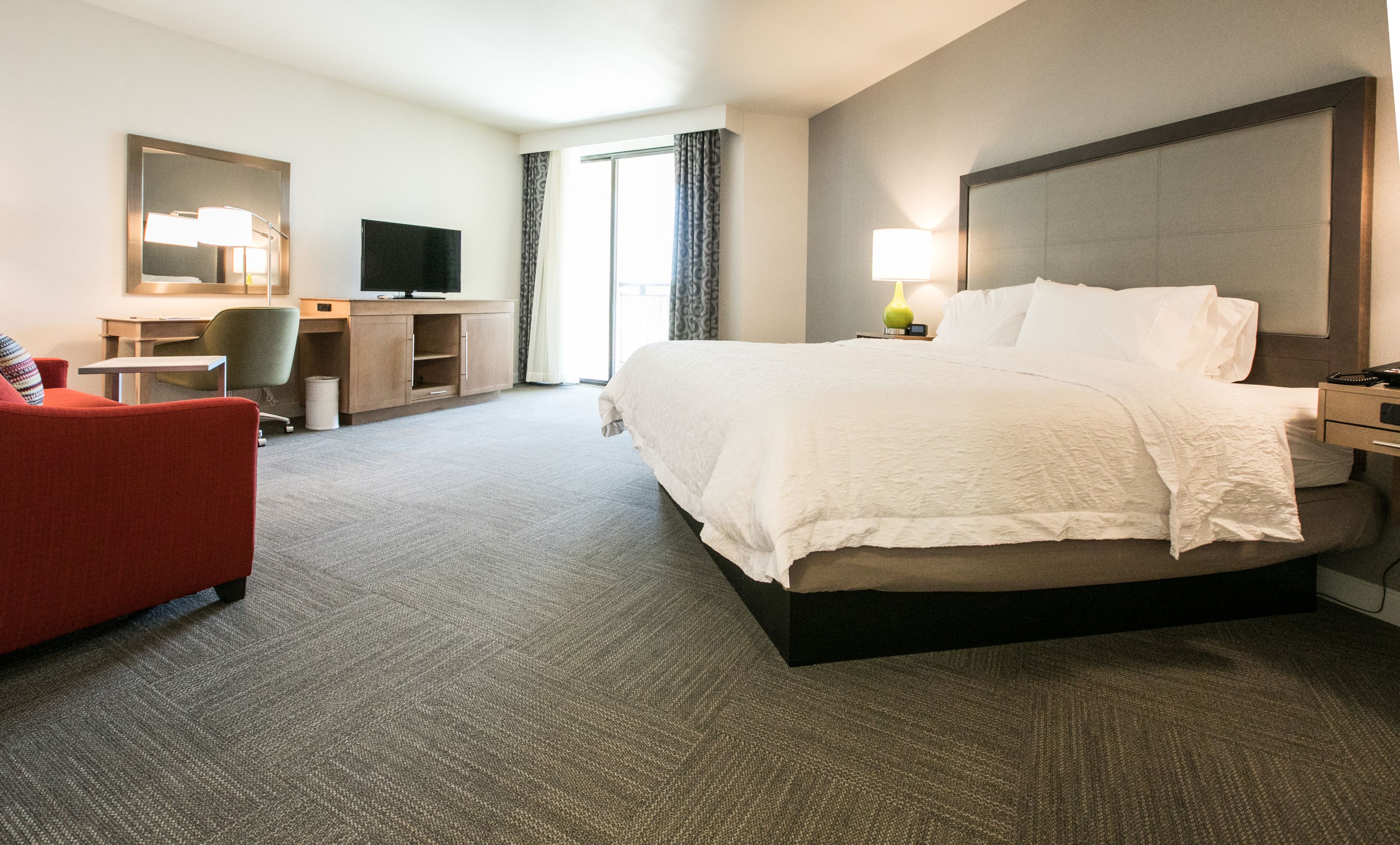 A hotel room with a large bed, a desk with a chair, a television, and a lamp.