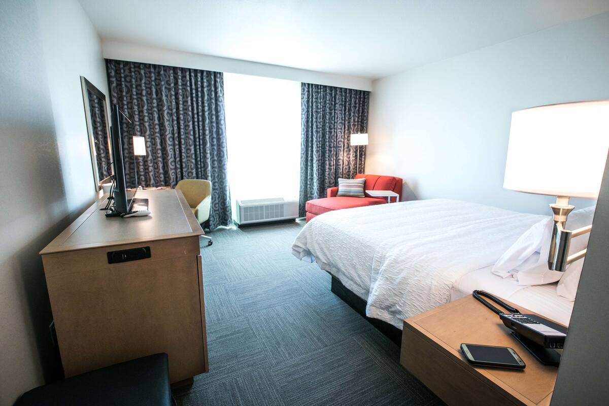 A hotel room with a bed, desk, chair, and a view of the outdoors.