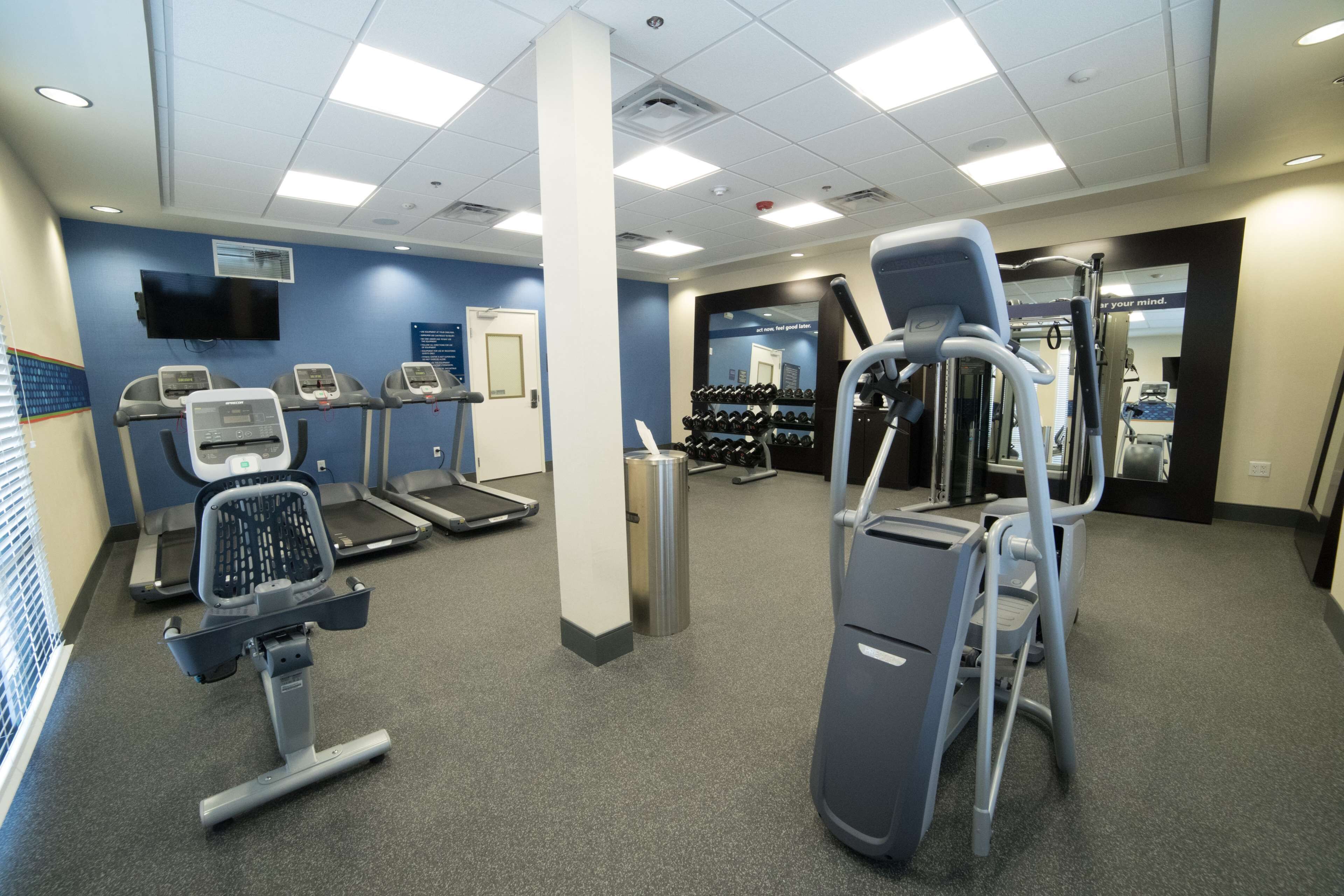 Un gimnasio con cintas de correr, elípticas y un soporte para pesas.