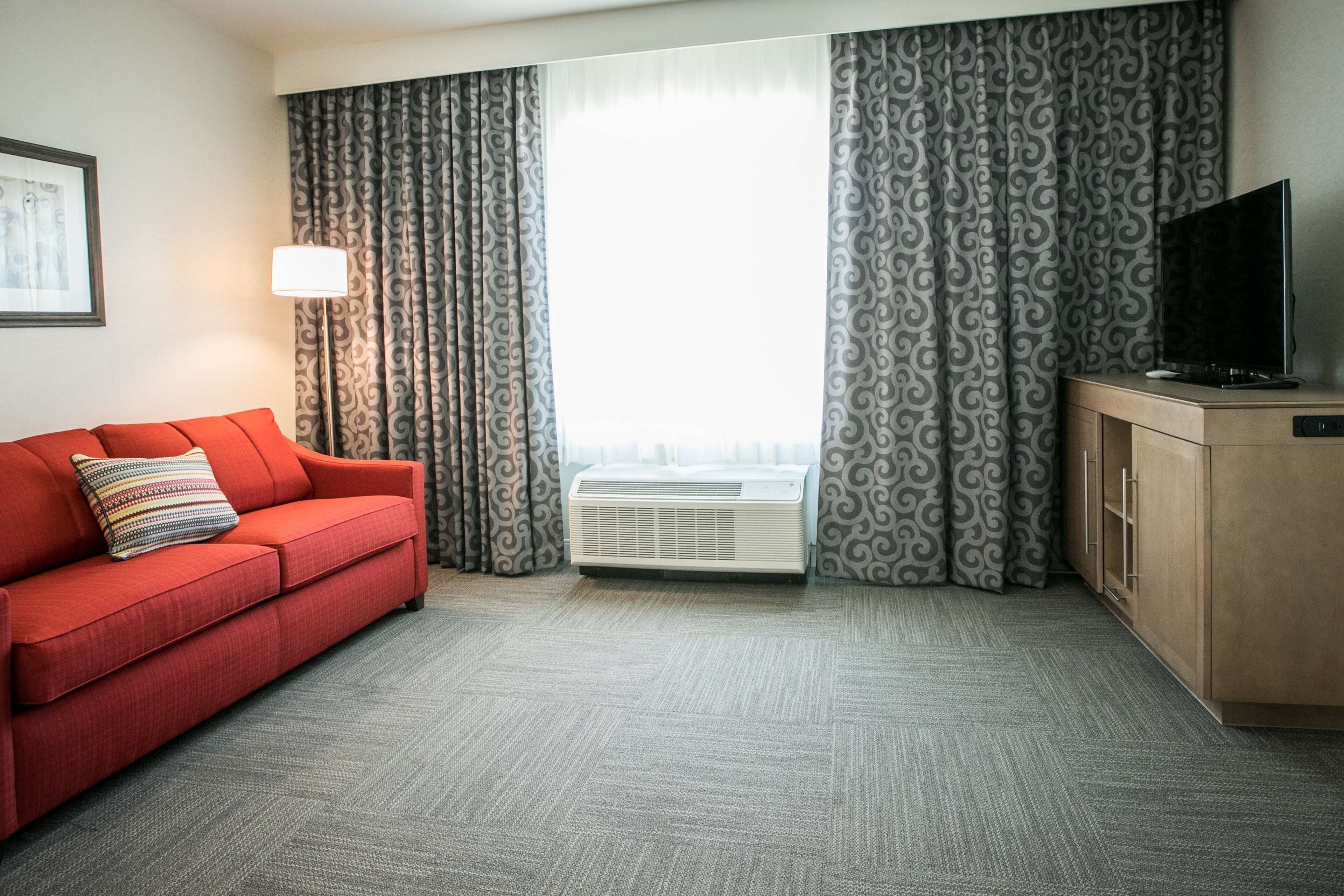 Une chambre d’hôtel avec un canapé rouge, un téléviseur posé sur un meuble en bois et des rideaux à motifs.