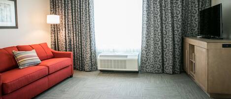 Une chambre d’hôtel avec un canapé rouge, un téléviseur posé sur un meuble en bois et des rideaux à motifs.