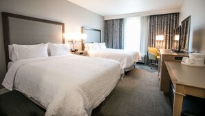 A hotel room with two beds, a desk, a chair, and a large window with curtains.