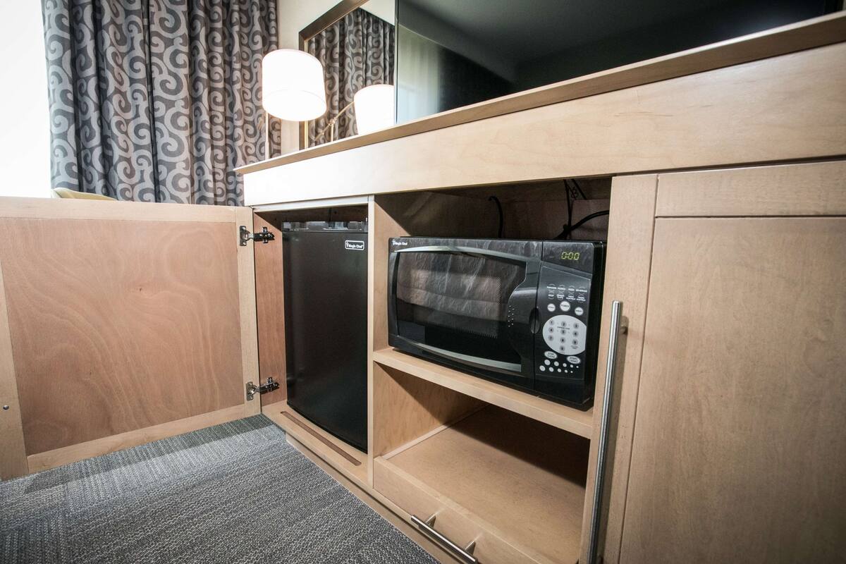 A compact kitchen with a microwave and a refrigerator built into wooden cabinetry.