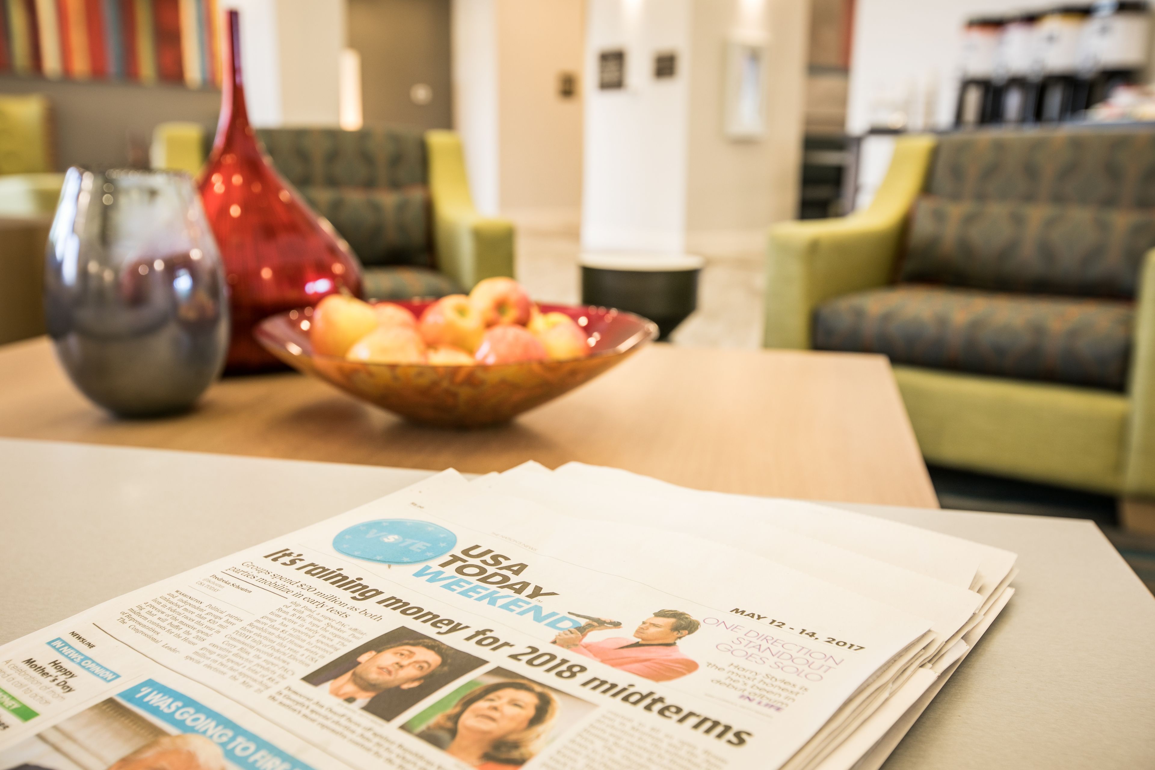 A USA Today newspaper on a table with a bowl of fruit and a vase.
