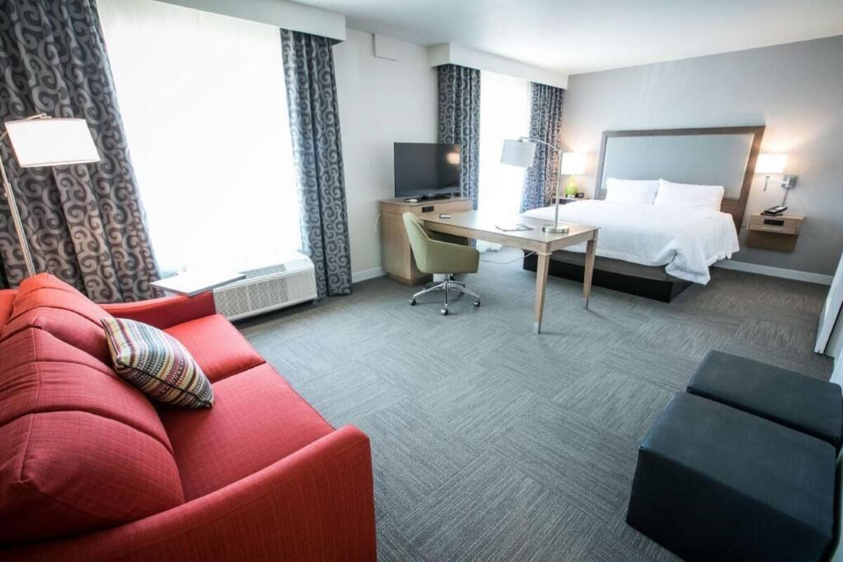 A hotel room with a red sofa, a desk, a bed, and a TV.